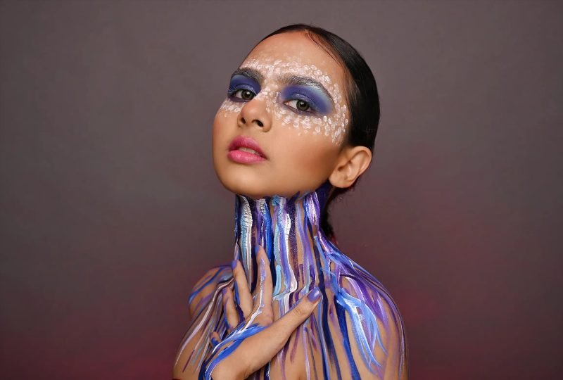 Editorial makeup: blue and purple paint running down the neck, the model looking upward